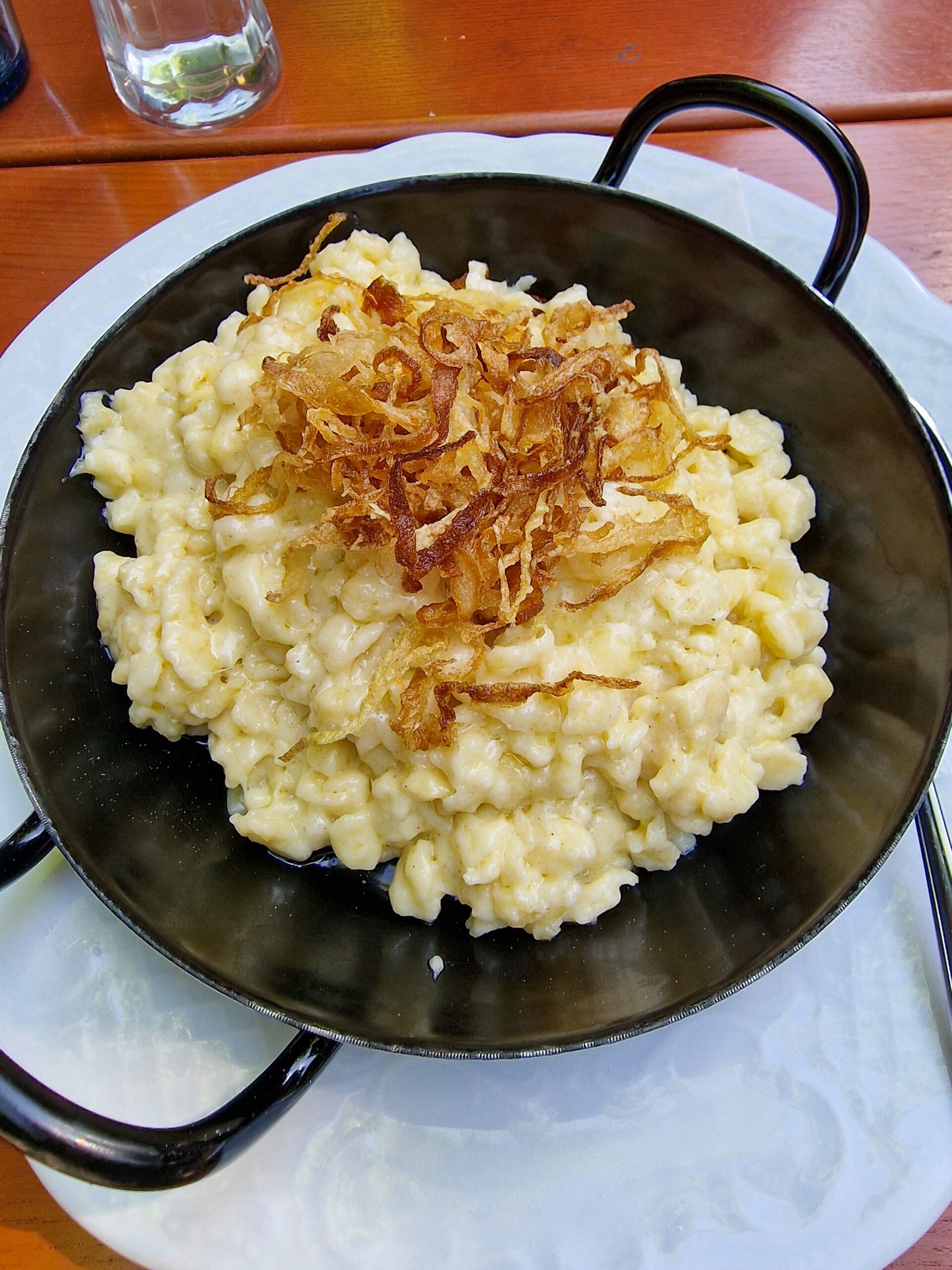 Guia de melhores restaurantes onde comer em Zurique 3 Aceitamos Viagens onde comer em zurique Um prato preto com Spätzle: macarrão com queijo e cebola frita.